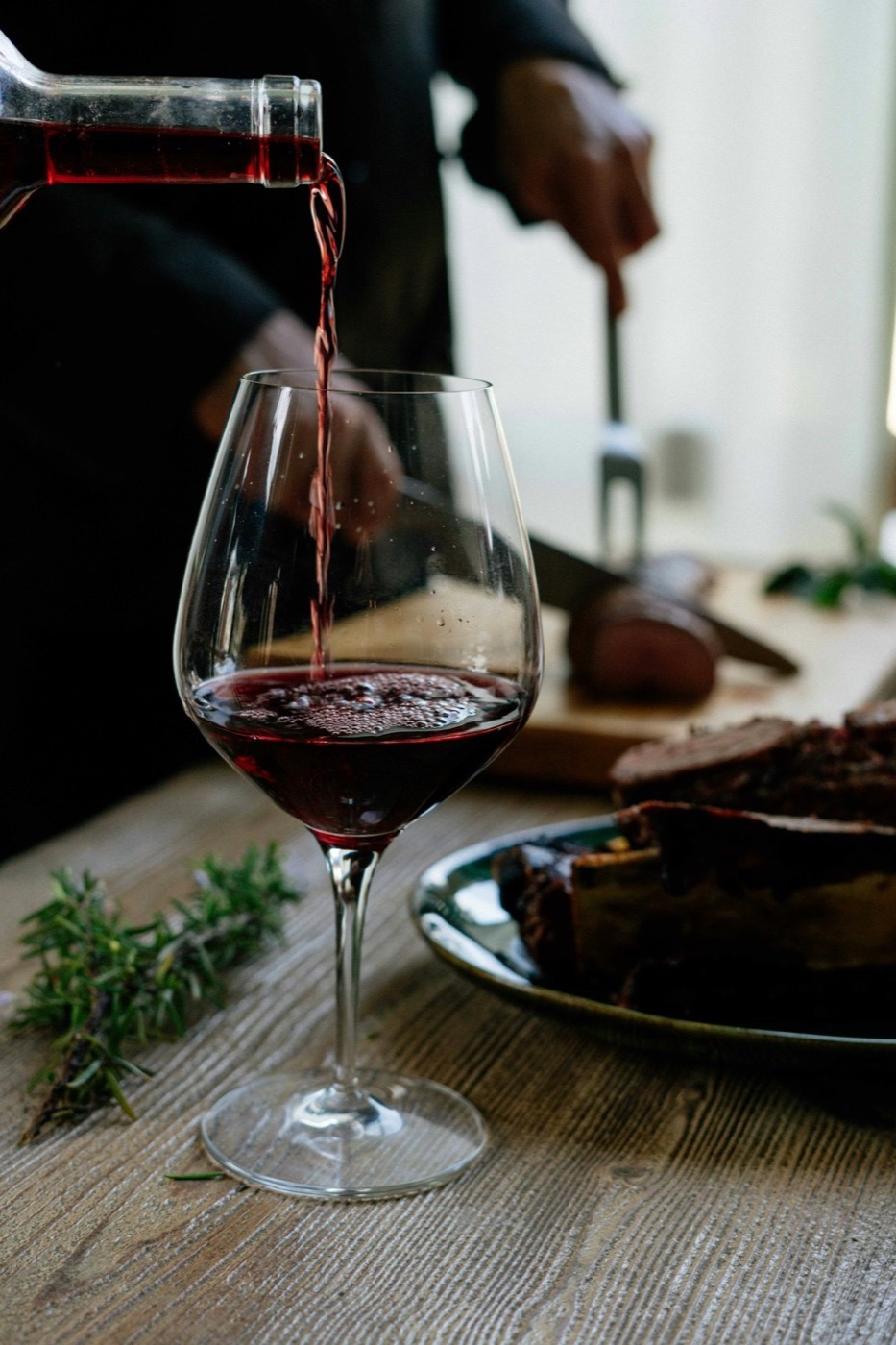 Red wine pouring into a glass over a rustic wood table